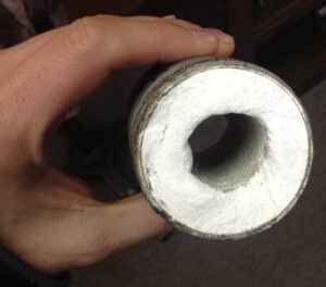 A pipe clogged by struvite held in a hand with a black background